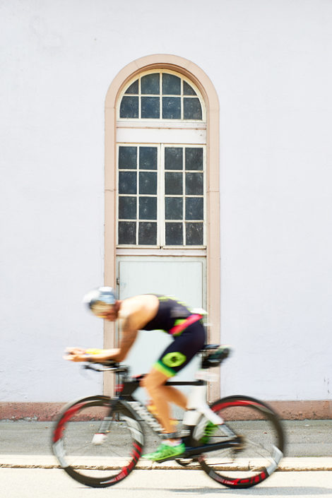 Triathlet auf dem Rad vor einem Gebäudefenster