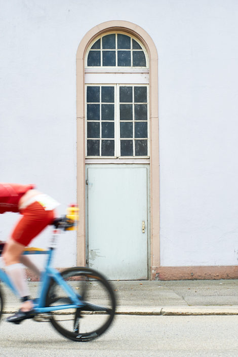 Triathlet auf dem Rad vor einer Fassade