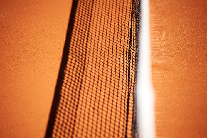 Der Schatten vom Tennisnetz auf dem Sandplatz