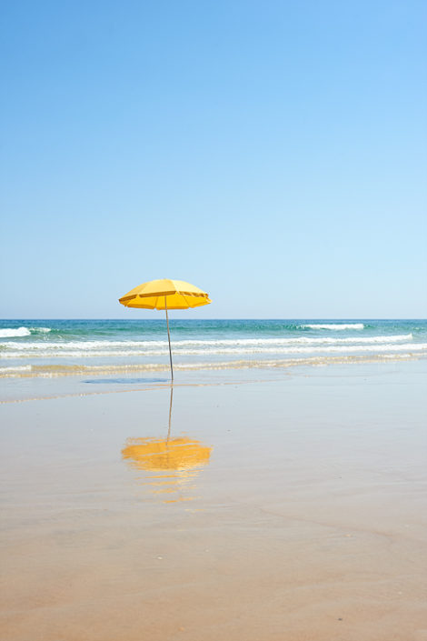 Ein gelber Sonnenschirm steht verloren im Wasser an einem flachen Sandstrand