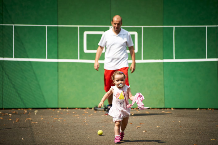 Ein kleines Mädchen und ihr Vater laufen von der Tenniswand weg