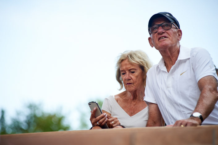 Eine Zuschauerin blickt auf ihr Smartphone und ihr Mann verfolgt das Spiel