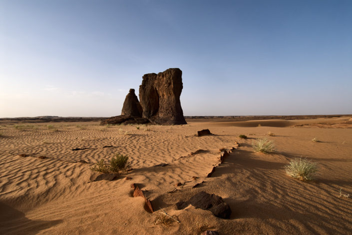 Drei Felssäulen im Abendlicht ragen aus dem Wüstensand empor