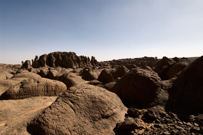 Wüstenboden mit runden Felsen und Felstürmen im Hintergrund