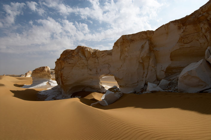 Eine Felsmauer mit einem Durchgang erhebt sich aus dem Sand