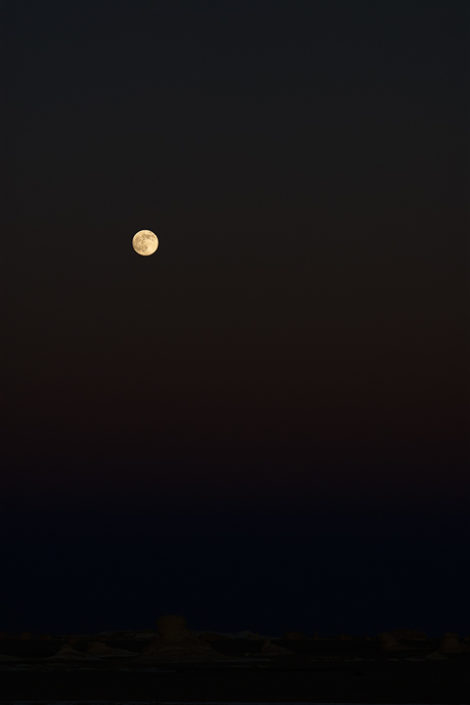 Der aufgegangene Mond wirft eine feines Licht auf den Wüstenboden