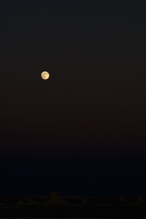 Der aufgegangene Mond wirft eine feines Licht auf den Wüstenboden