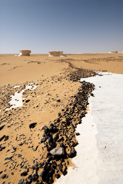 Schwarze Steine und Sand bedecken den weissen Wüstenboden